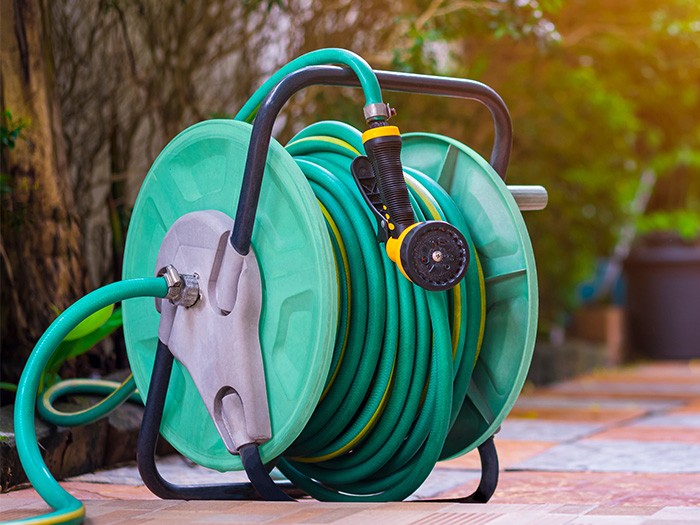 Green Garden Hose Corral on bricked patio floor. 